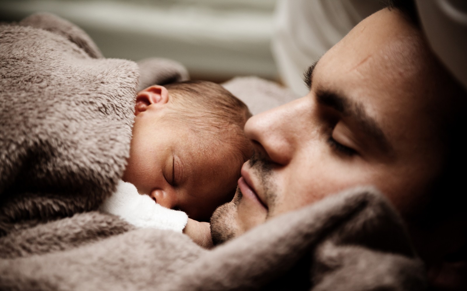 Newborn and father asleep In bed