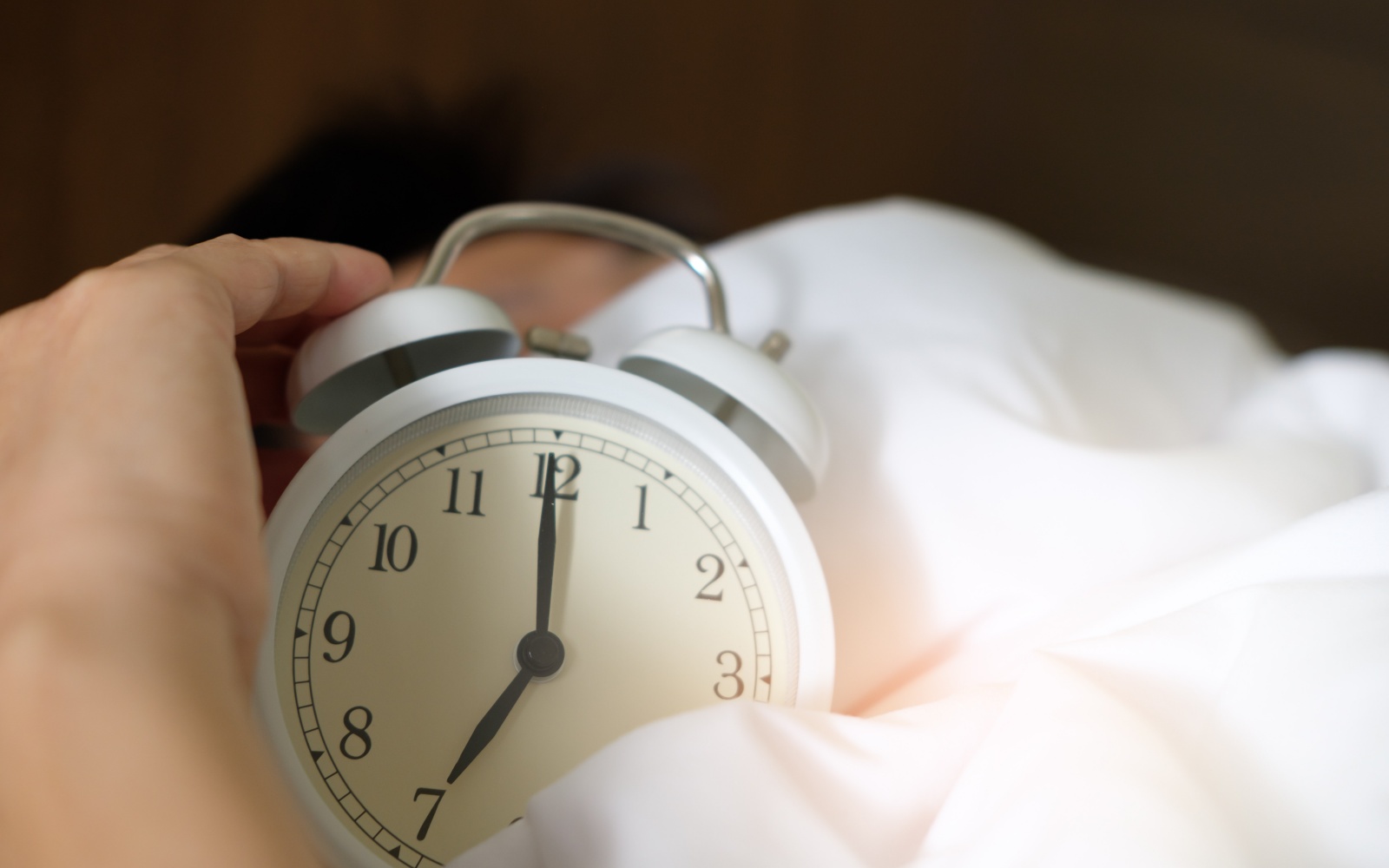 Person in bed holding alarm clock for feature on how long we should sleep